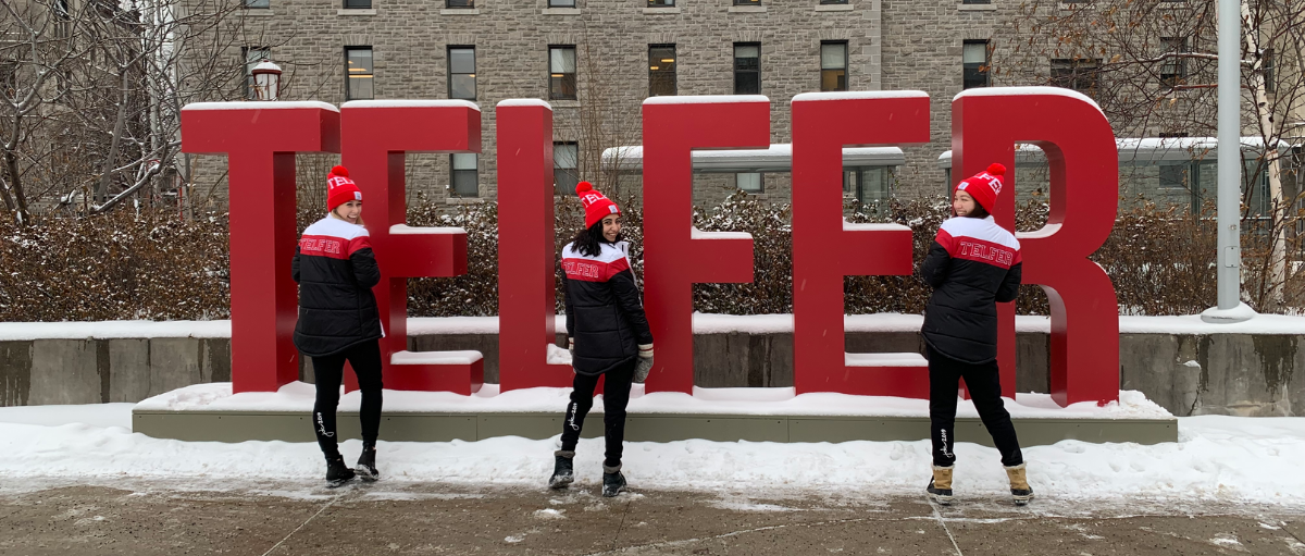 three students smiling in front of the telfer sign