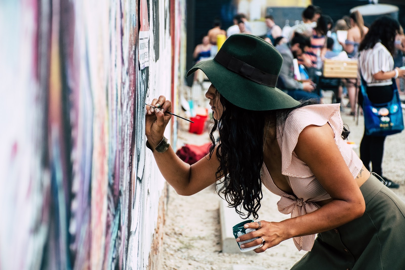 Une femme avec un chapeau fait de l'art à la peinture sur un mur extérieur