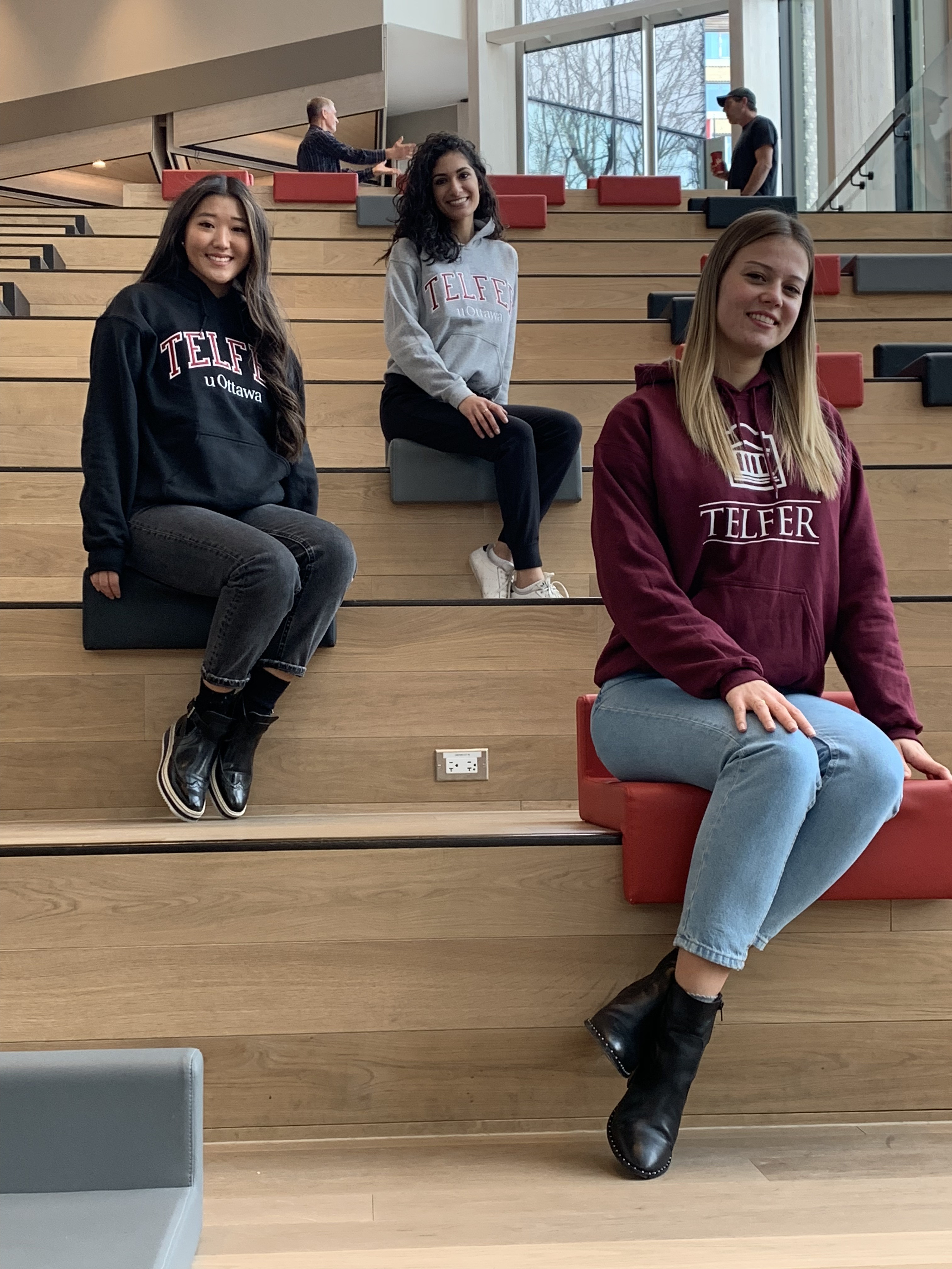 three Telfer students sitting on stairs smiling, wearing Telfer apparel