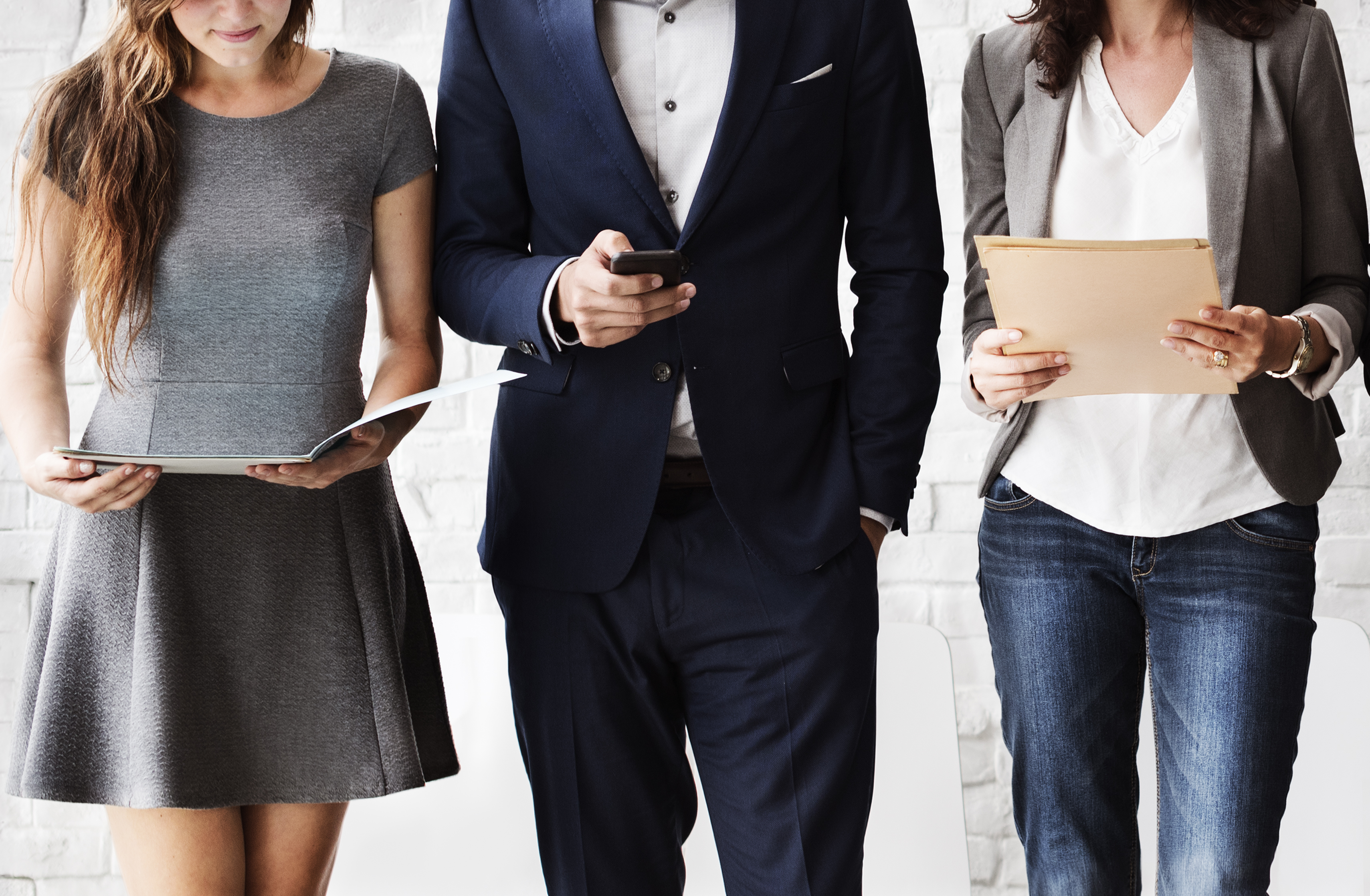 Two women and a man walking together. The man is looking at a cellphone