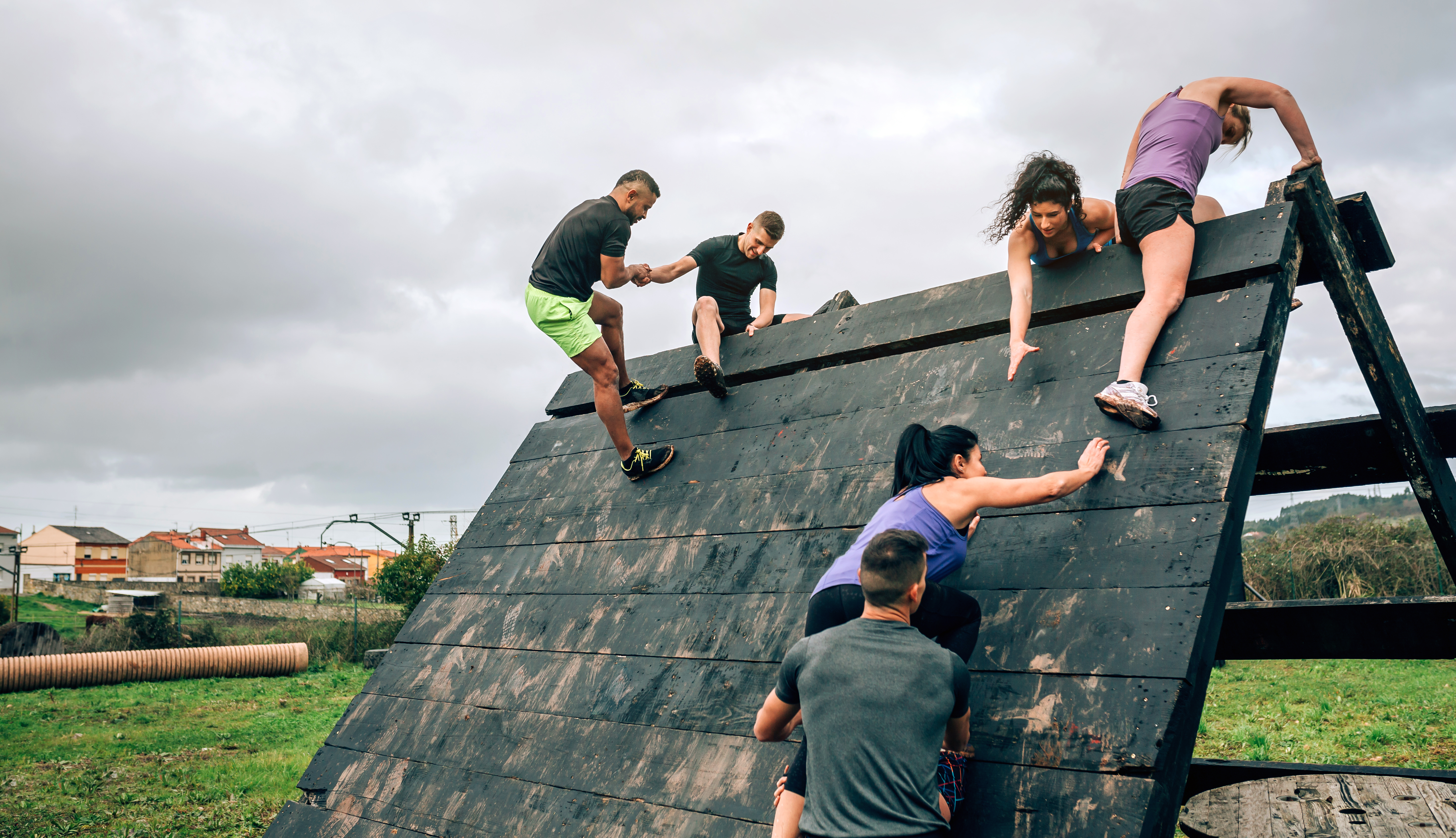 people helping eachother over an obstacle course wall