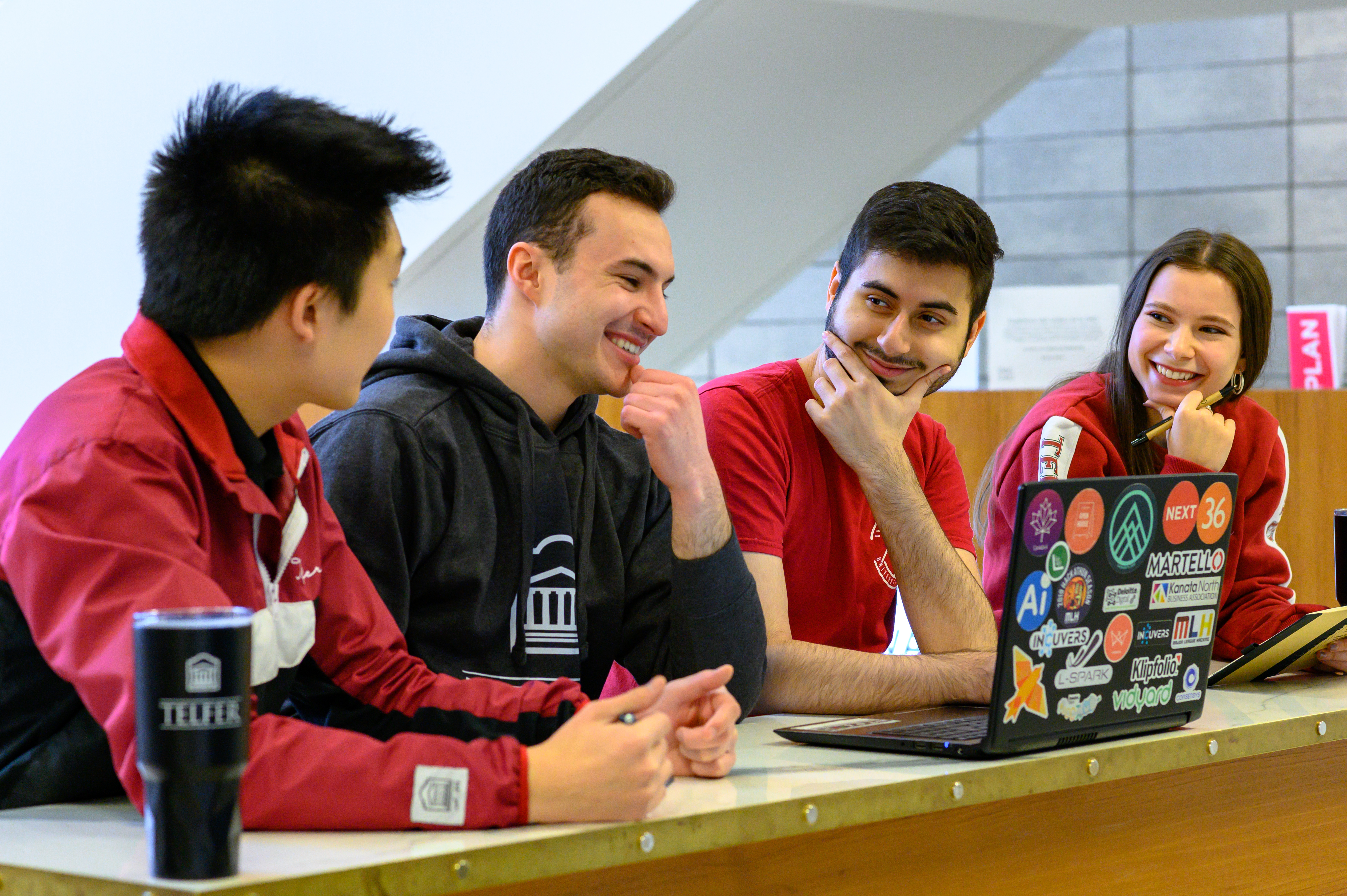 Quatre étudiants de Telfer se souriant les uns aux autres en faisant une pause dans leurs études, assis à un bureau.