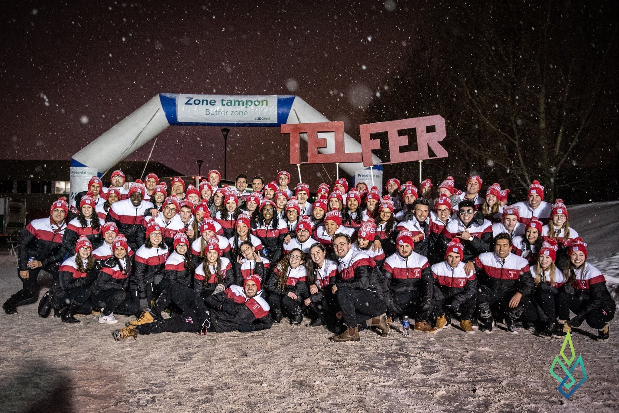 A group of students sitting in the snow holding up a Telfer sign