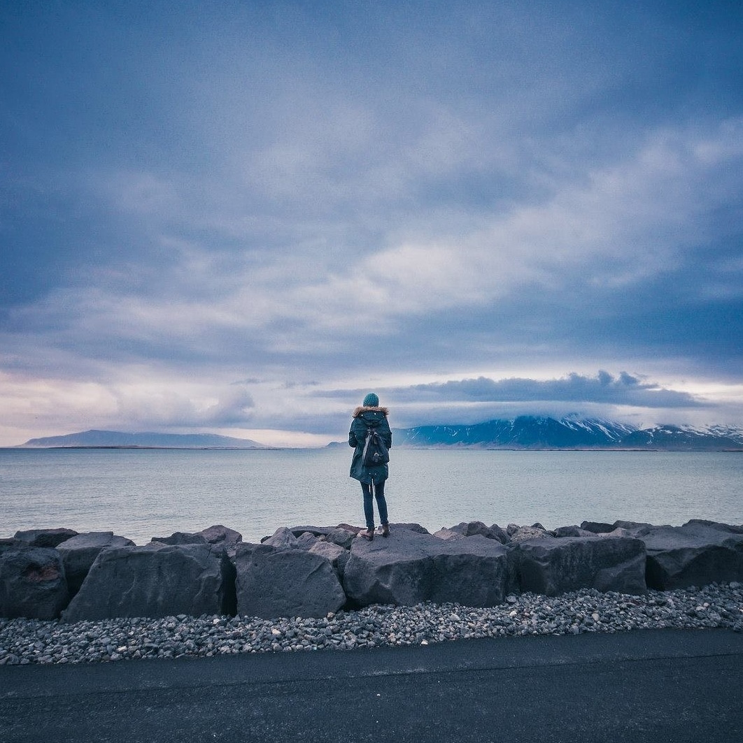 une personne sur des roches regardant un paysage de lac et montagnes