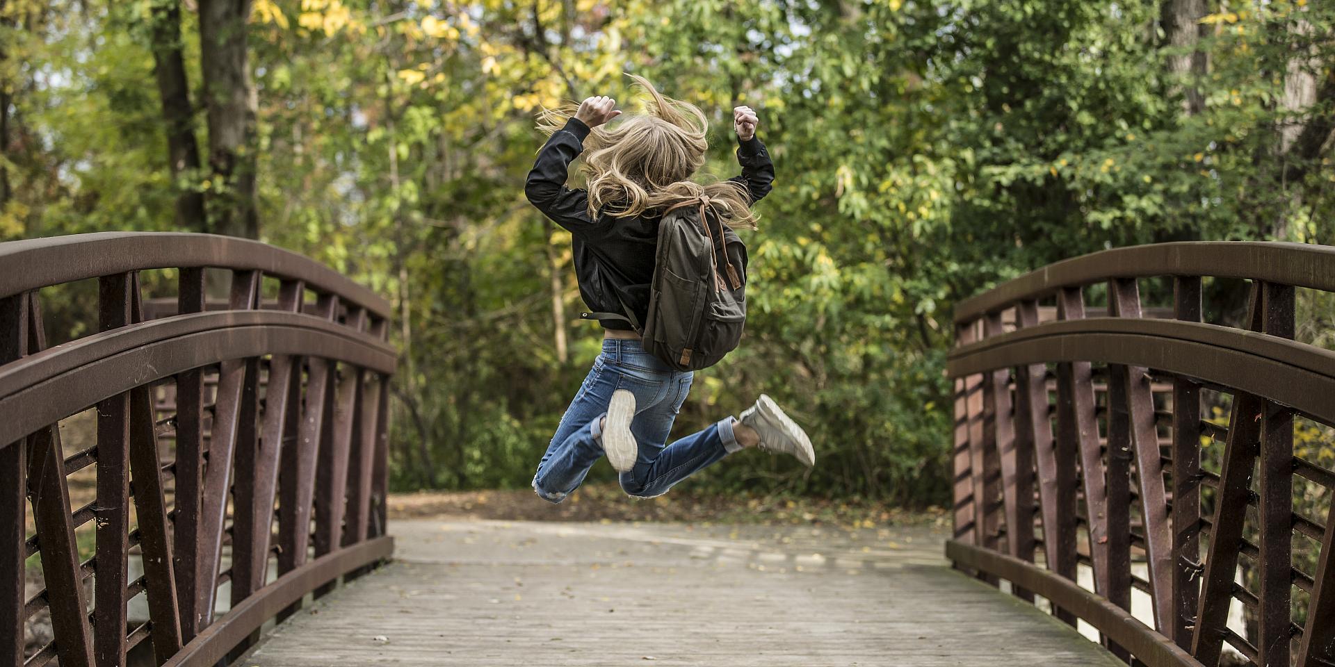 Une femme saute de joie sur un pont en nature