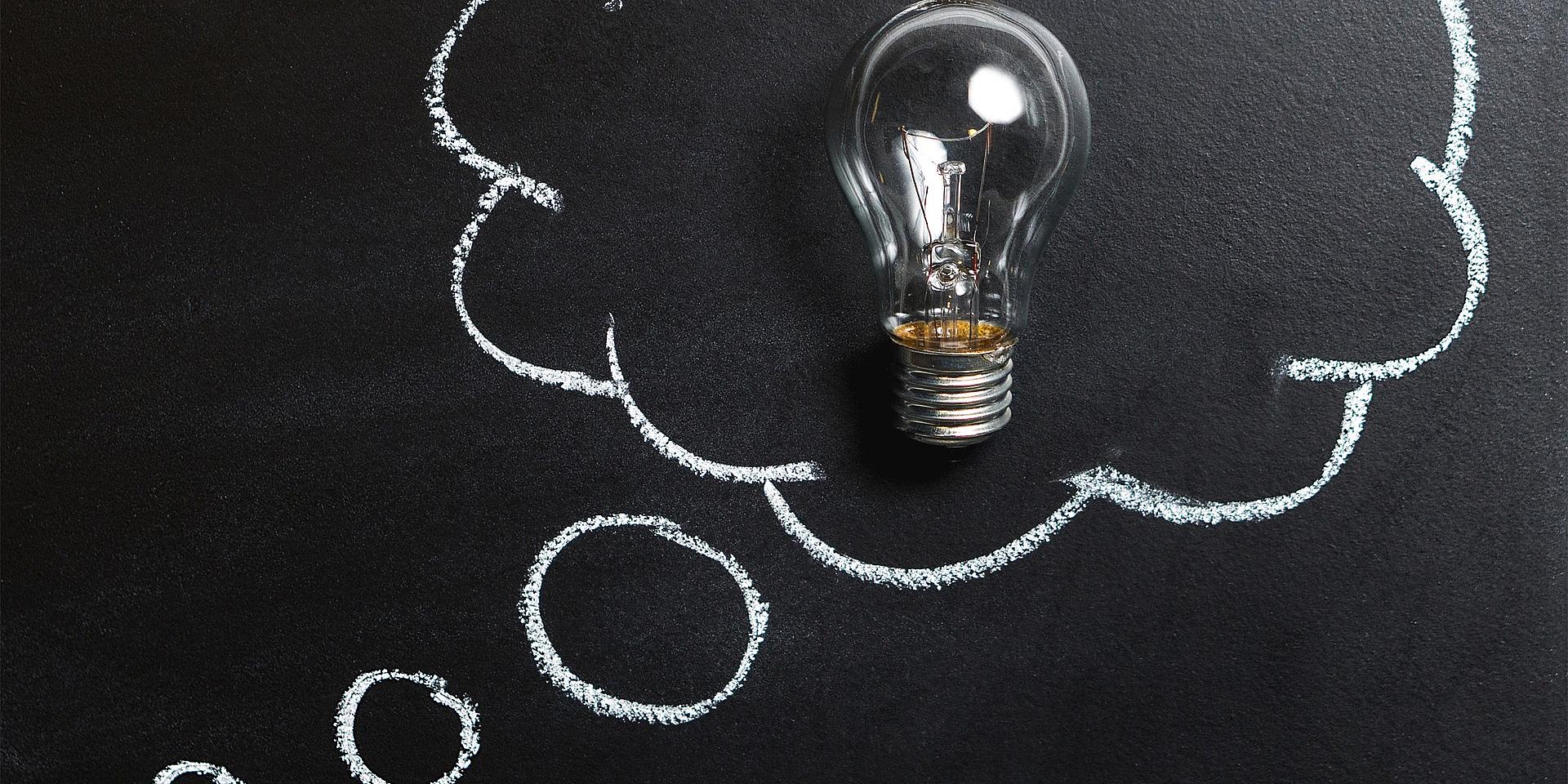 Lightbulb on a black board with a thought cloud drawn around it.