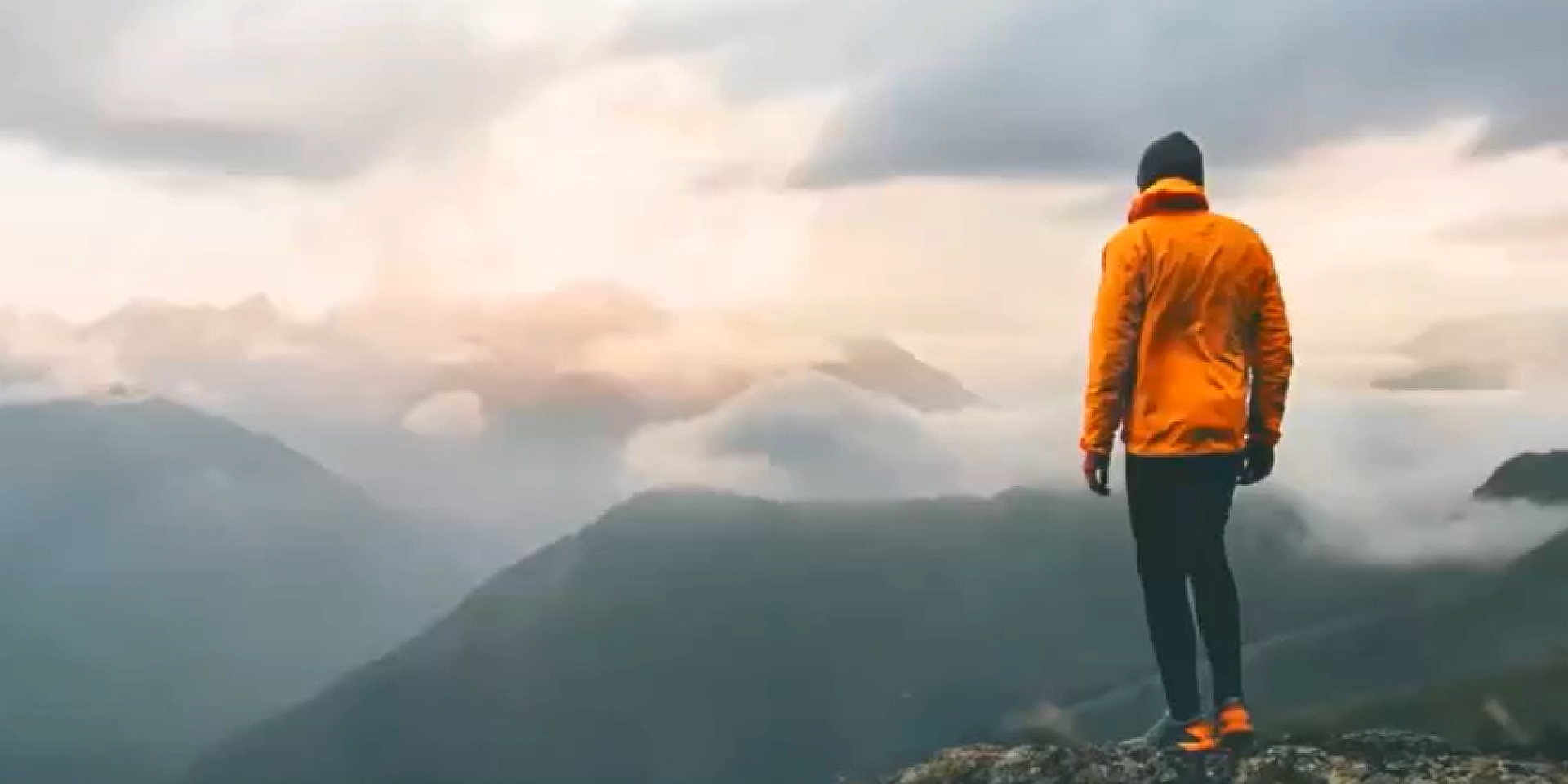 Homme habillé en orange au sommet d'une montagne