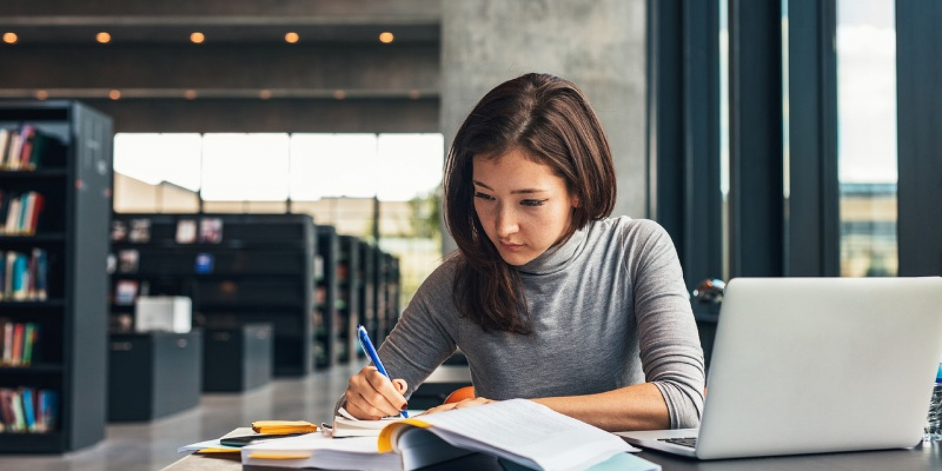 Student studying in the library with her laptop and books