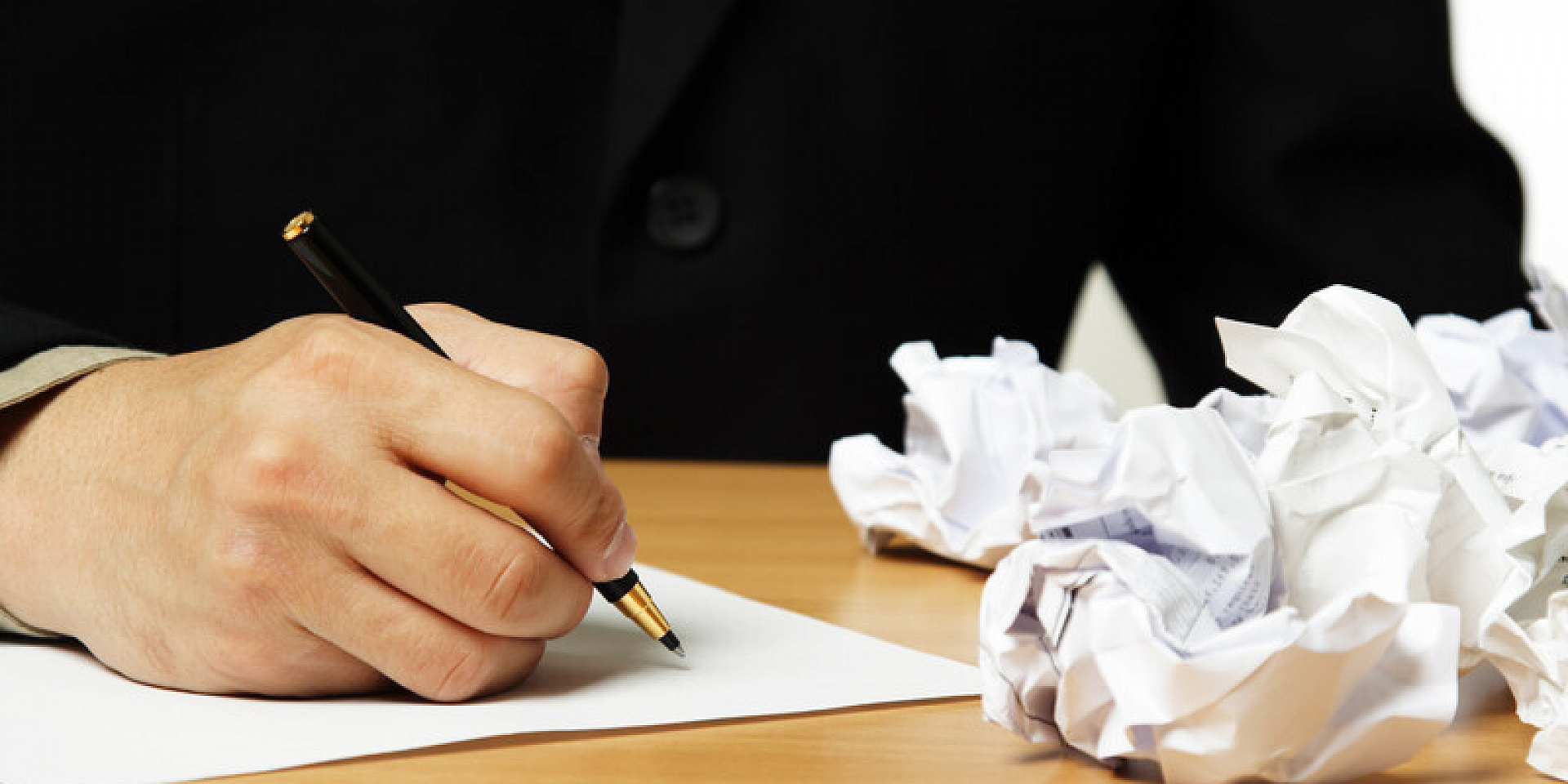 Homme écrit avec un stylo sur une feuille à côté de brouillons frippés