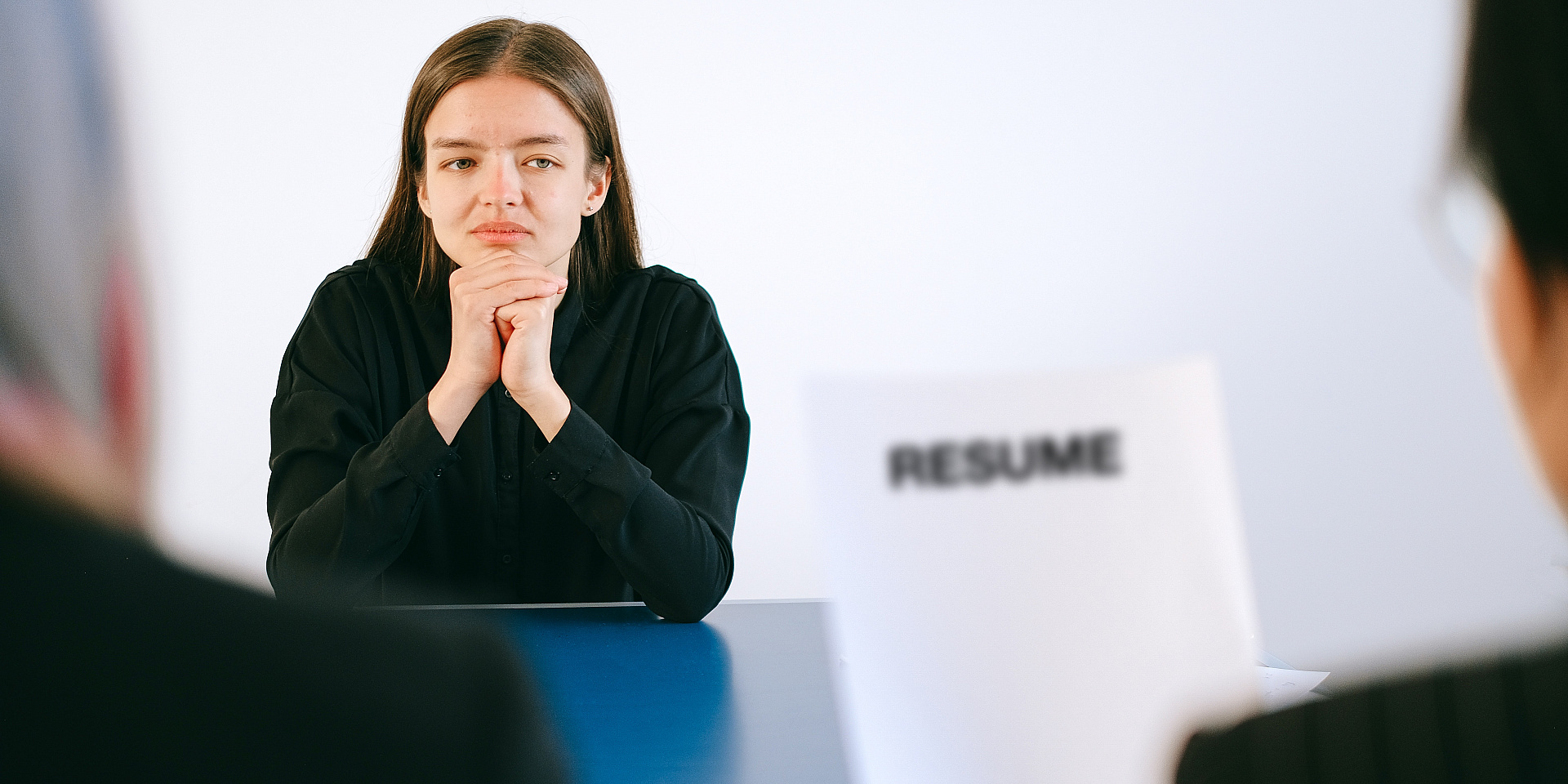 Woman waiting as two individuals read a paper with the word "Resume" on it