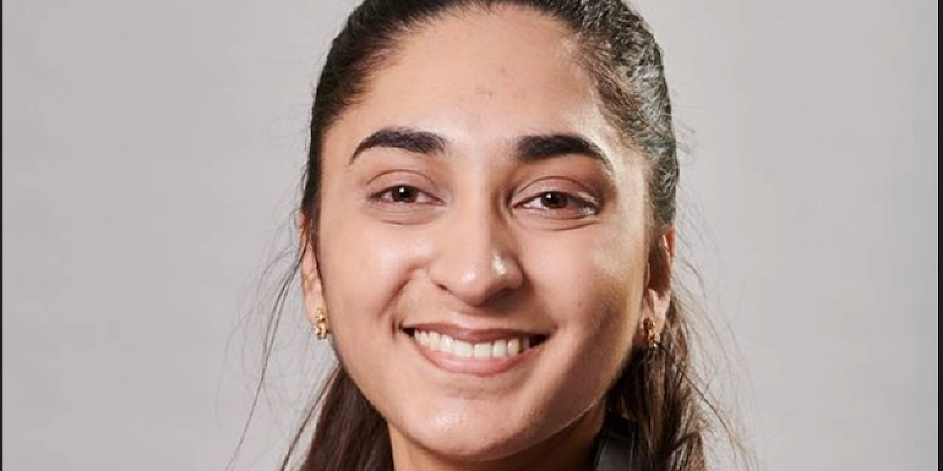 Maneesha Rakhra smiling in front of a grey background.