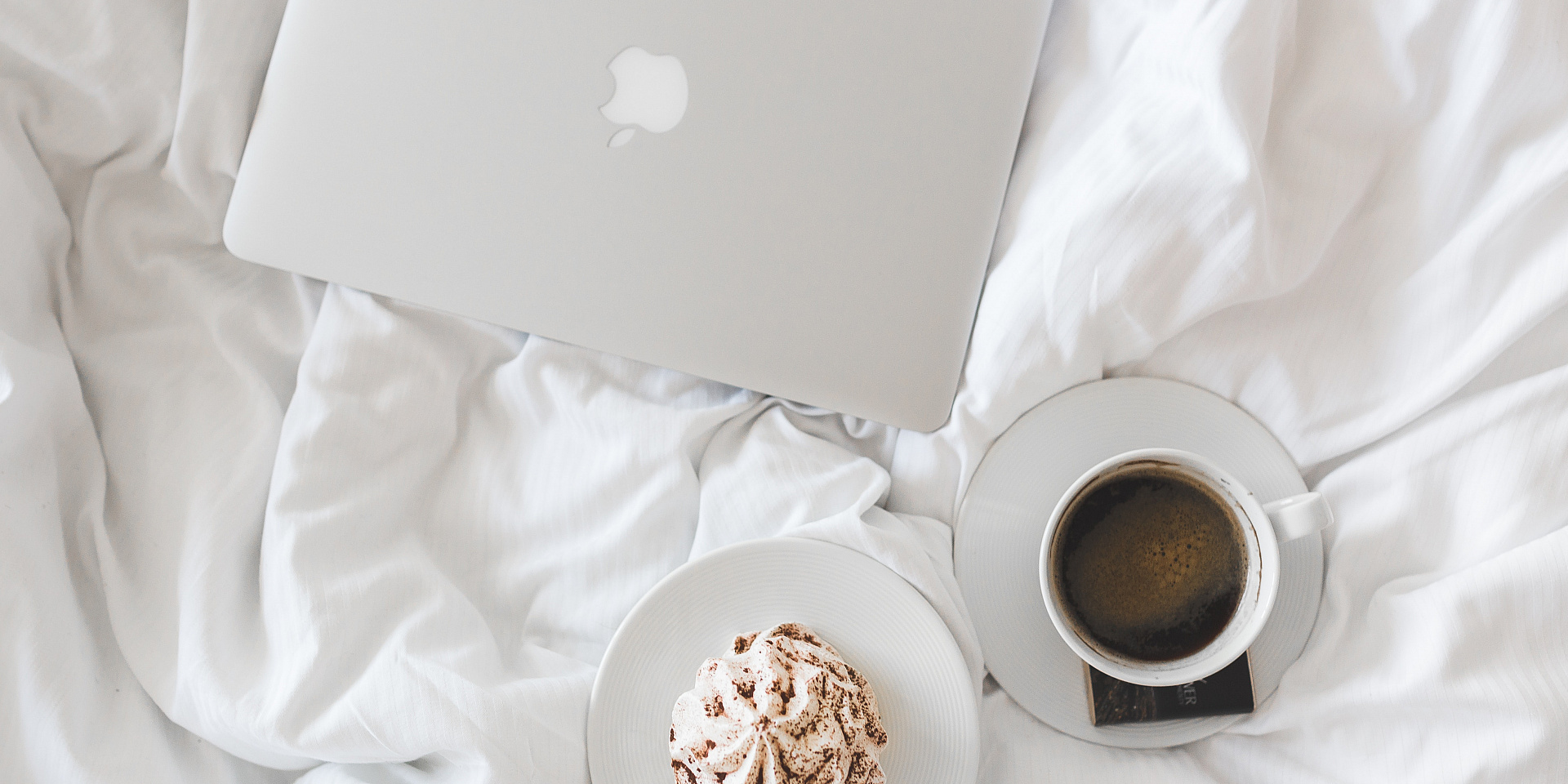 Laptop, coffee cup and cupcake on a bed.