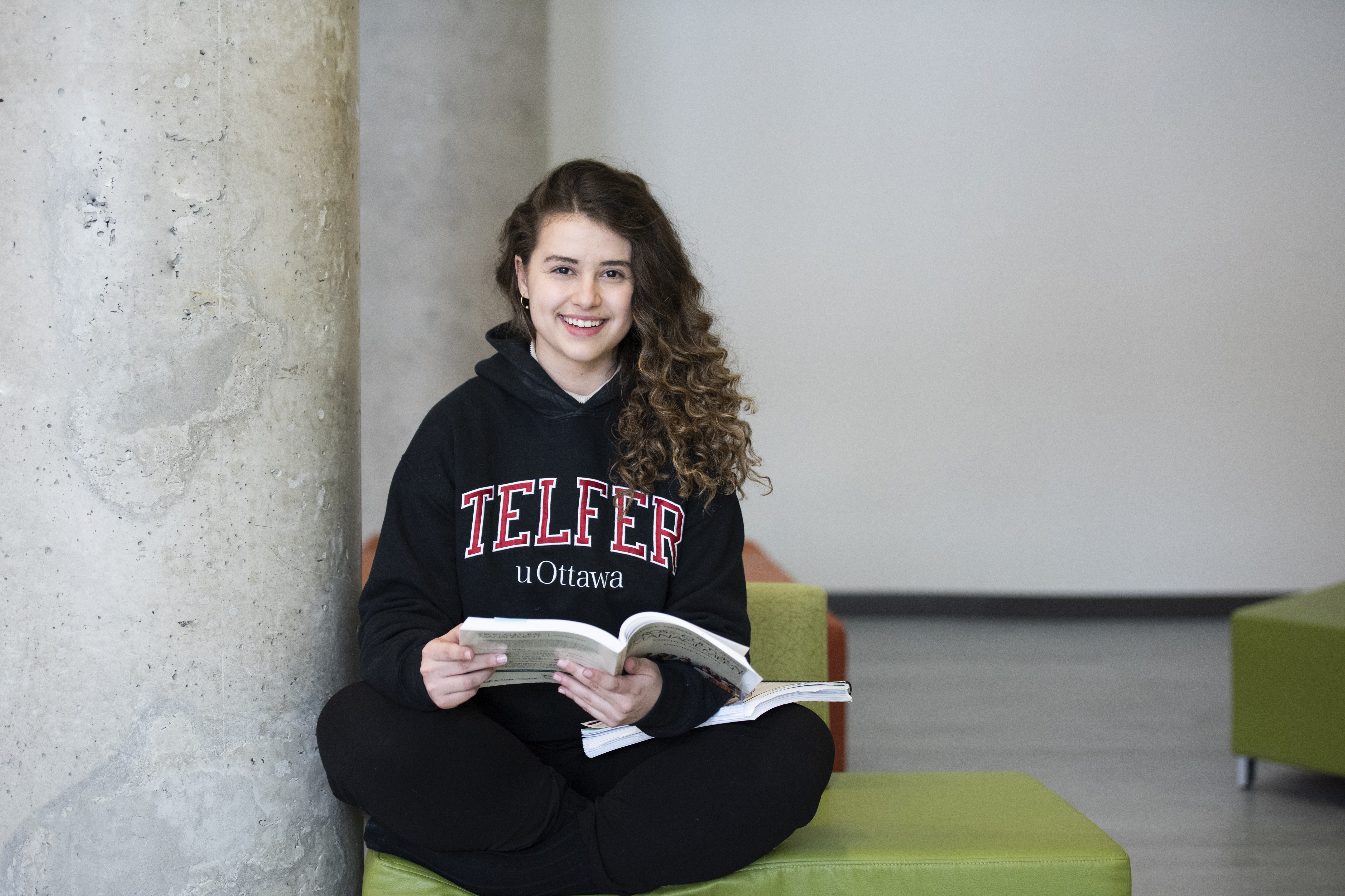 Smiling girl sitting on the floor of a study space with a book
