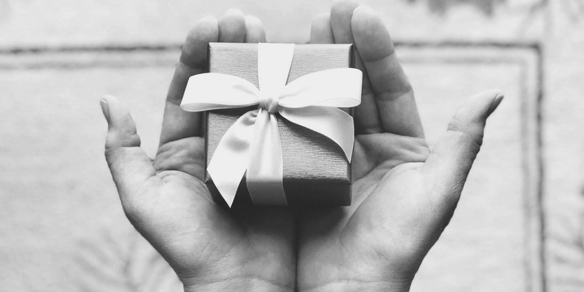 Black and white picture of a pair of hands holding a gift box with a bow