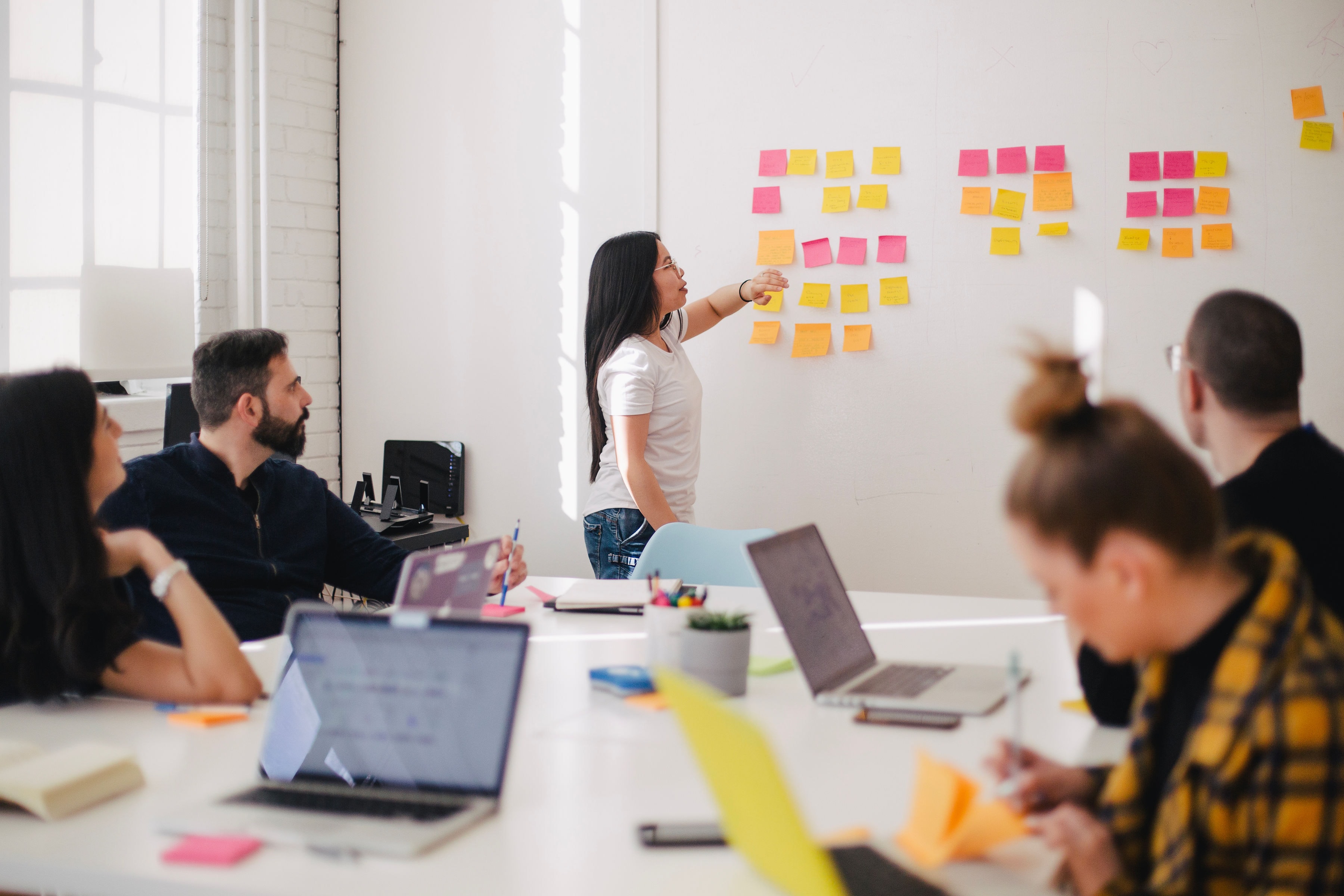 Students in a room working and listening to a presenter with post-its on a bord