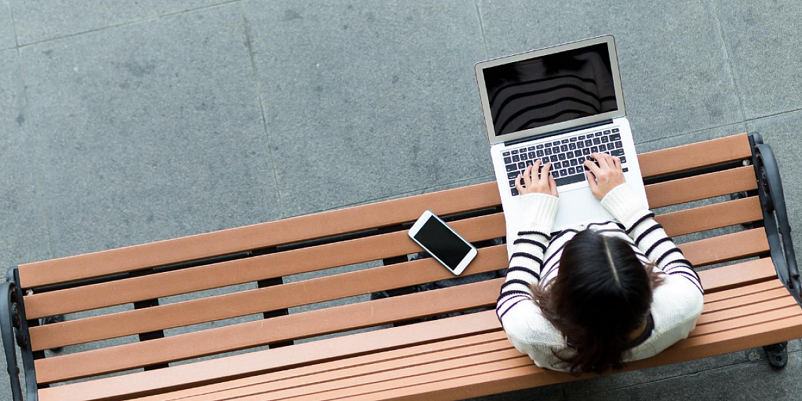 une étudiante travaillant sur son laptop alors qu'elle est assise sur un banc à l'extérieur
