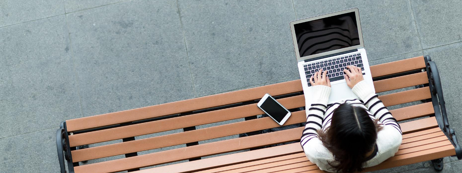 une étudiante travaillant sur son laptop alors qu'elle est assise sur un banc à l'extérieur