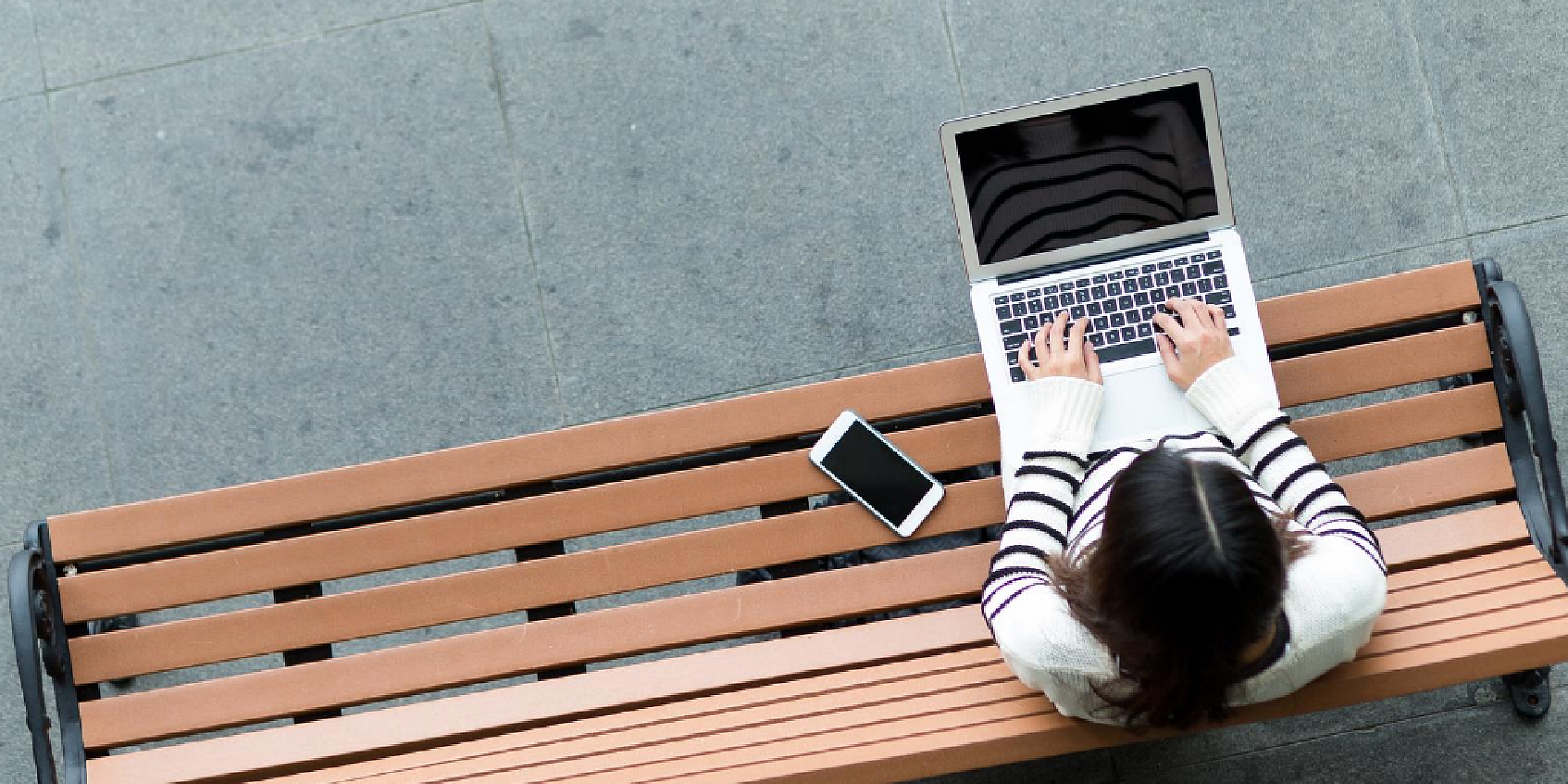 student working on their laptop while sitting on a bench outside