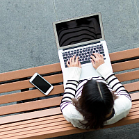 student working on their laptop while sitting on a bench outside