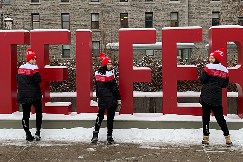 three students smiling in front of the telfer sign