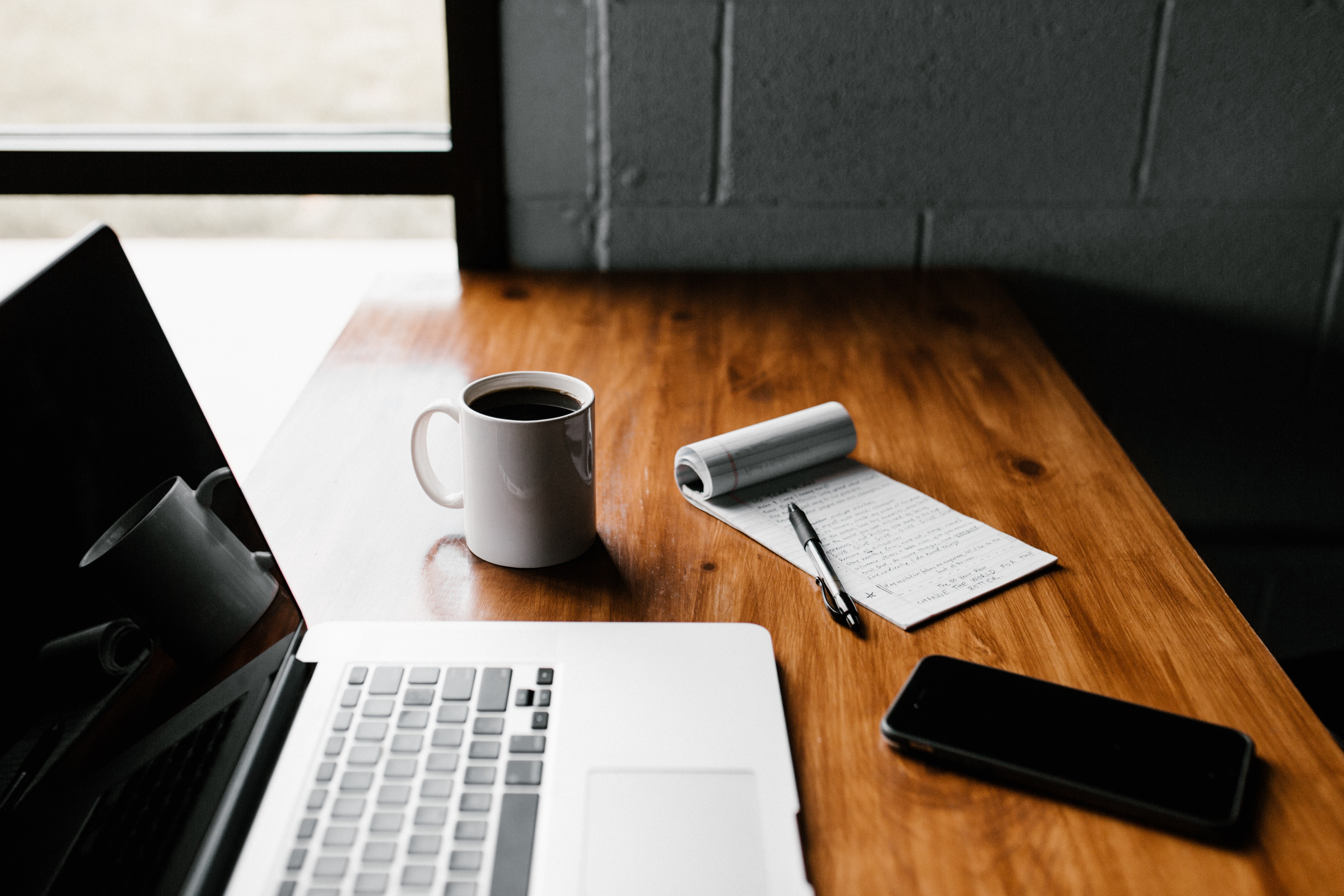 Laptop with coffee, notepad and cell phone on a table