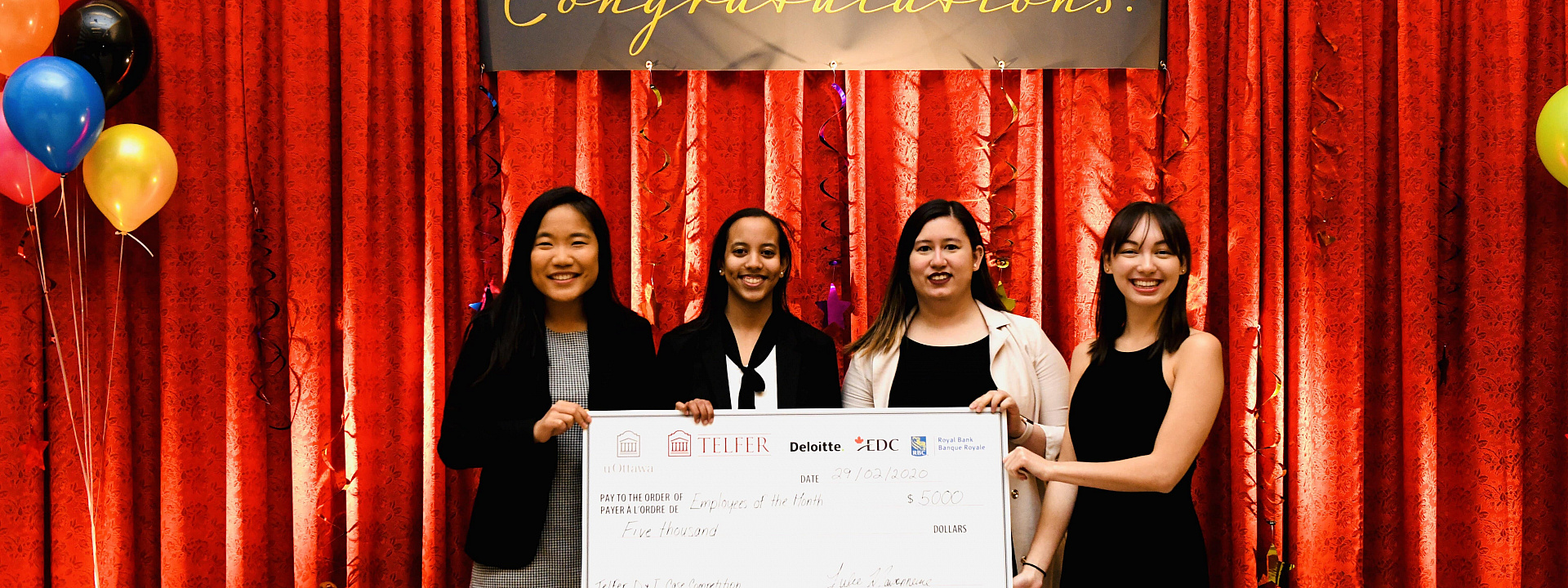 4 young happy women holding a big mock cheque in front of a red curtain