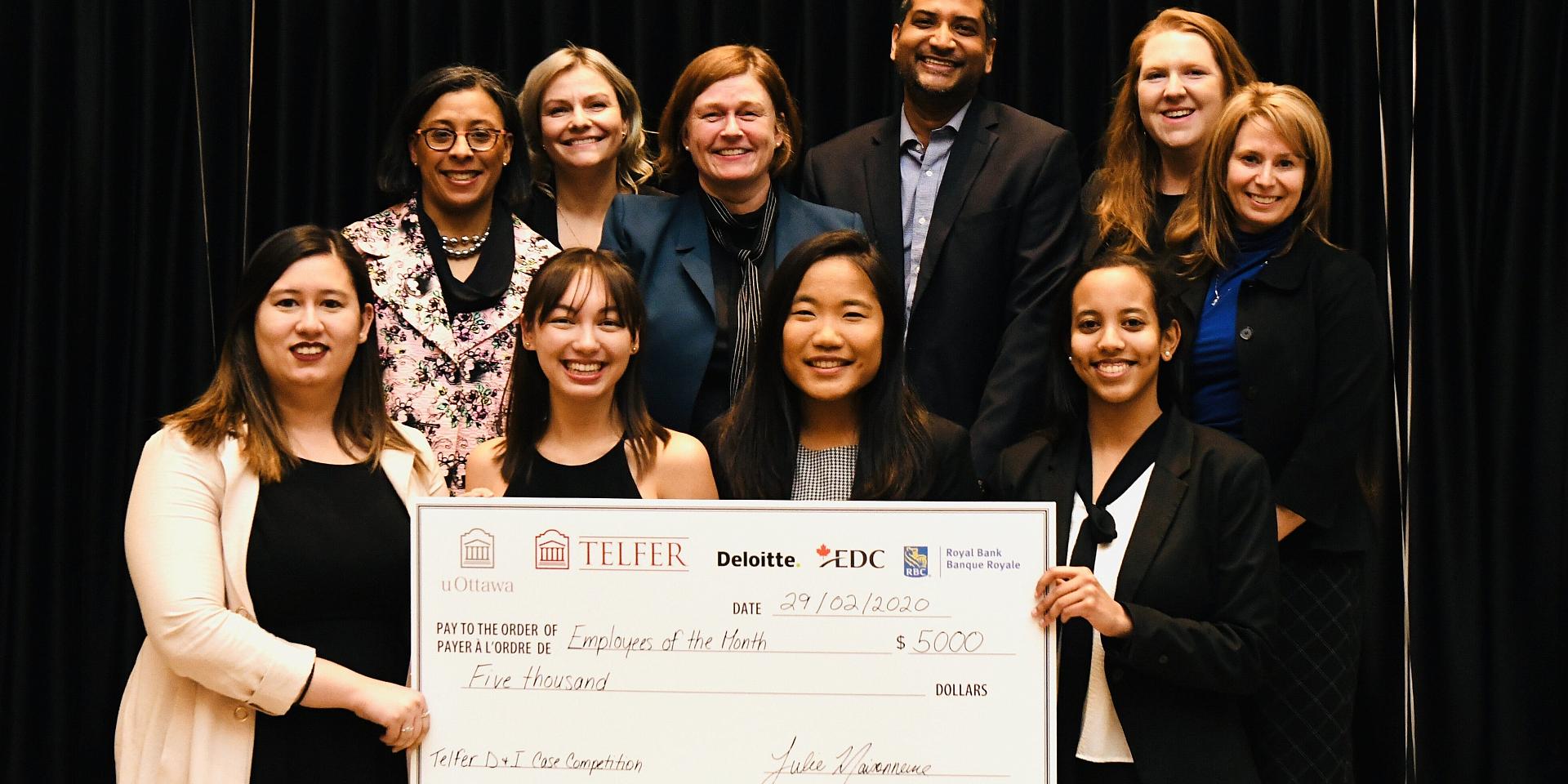 4 young happy women holding a big mock cheque surrounded by older smiling peoplein front of a black urtain