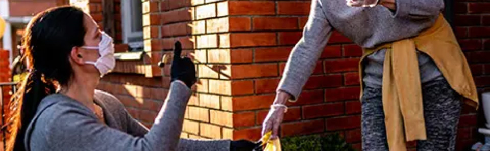 Woman handing grocery bag to an older woman