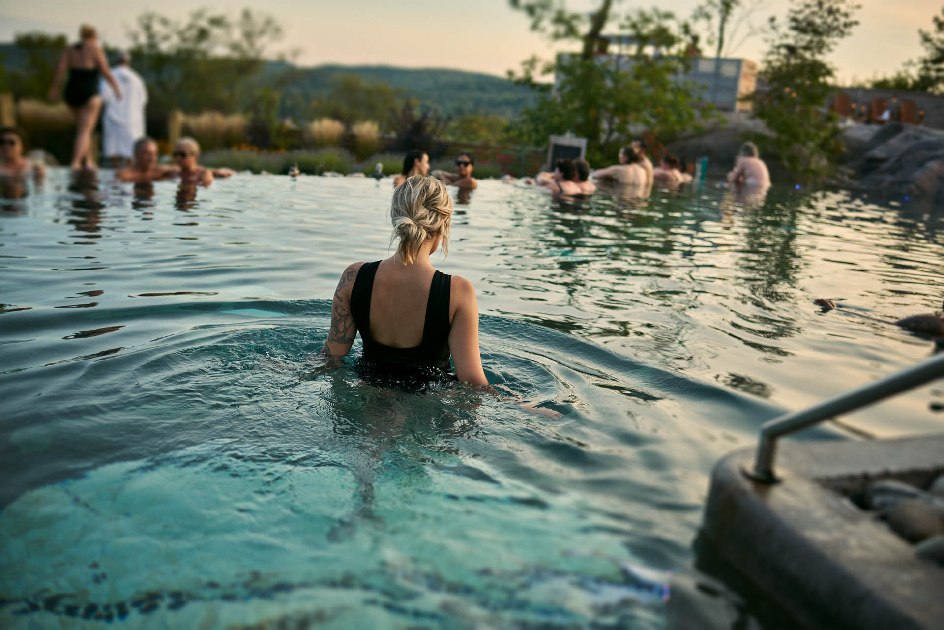 Femme se baignant dans la piscine infinie avec d'autres personnes en arrière-plan au Nordik Spa Nature