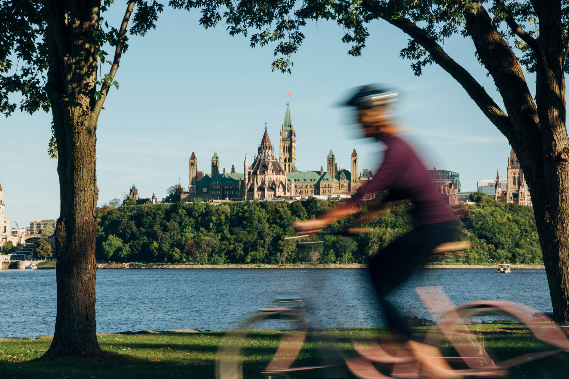 Femme floue à vélo de l'autre côté de la Rivière des Outaouais, avec la colline du Parlement en arrière-plan