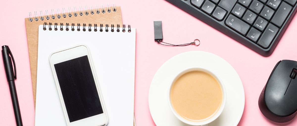 desk setup with phone, notepad, coffee, keyboard, and computer mouse