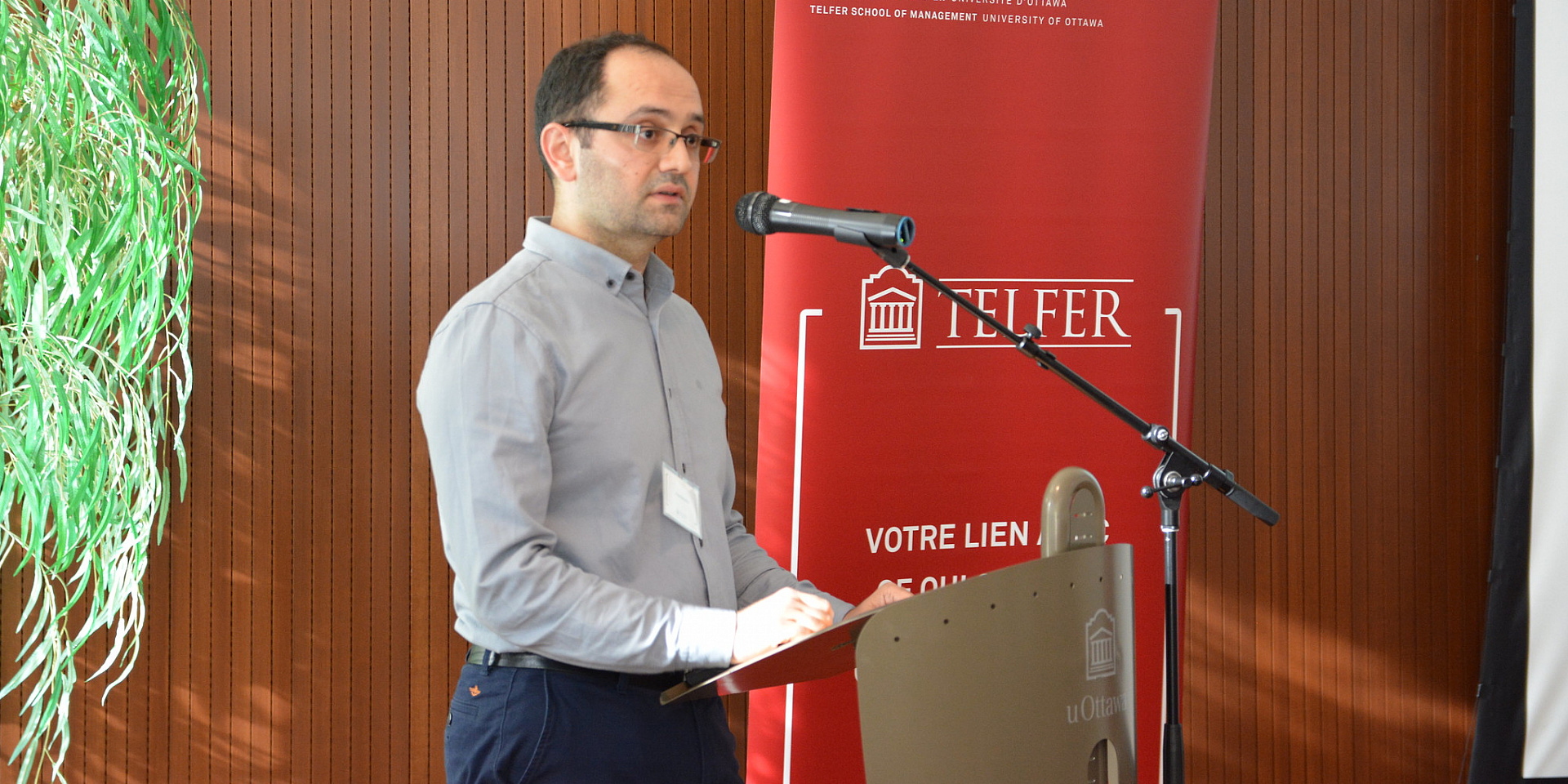 Speaker talking to a group. The speaker is standing near a telfer banner