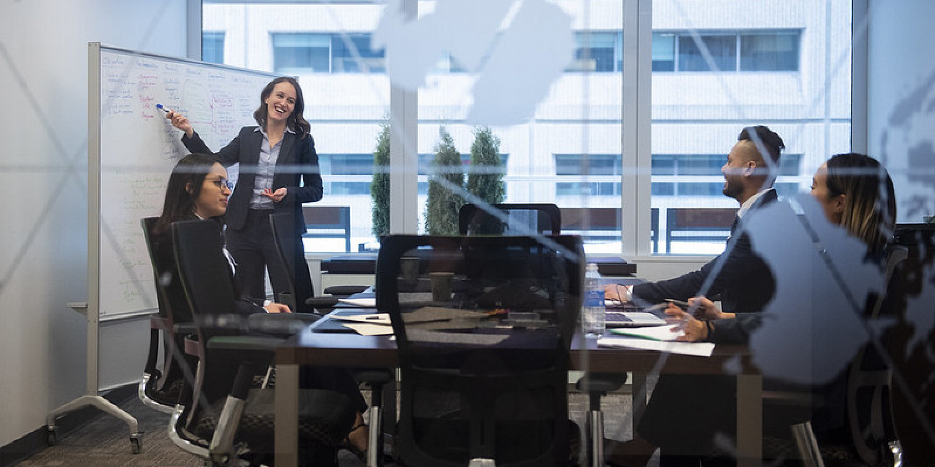 Woman writing on a white board in a meeting with colleagues