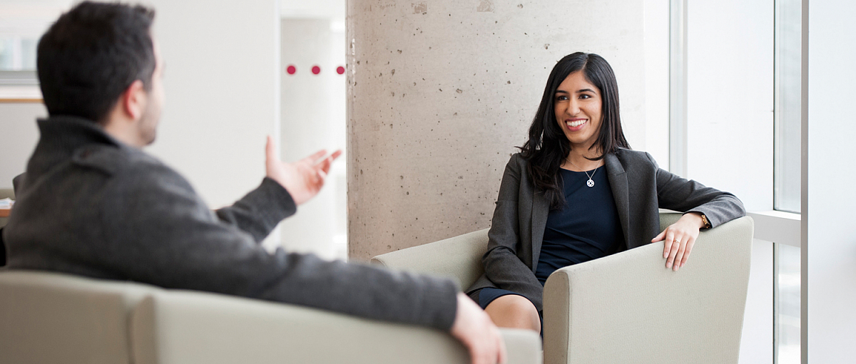 Two students, one clearly smiling, in lounge chairs having a conversation.