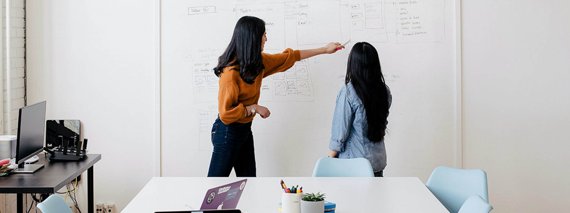 Two women working on a white board in a brainstorm session