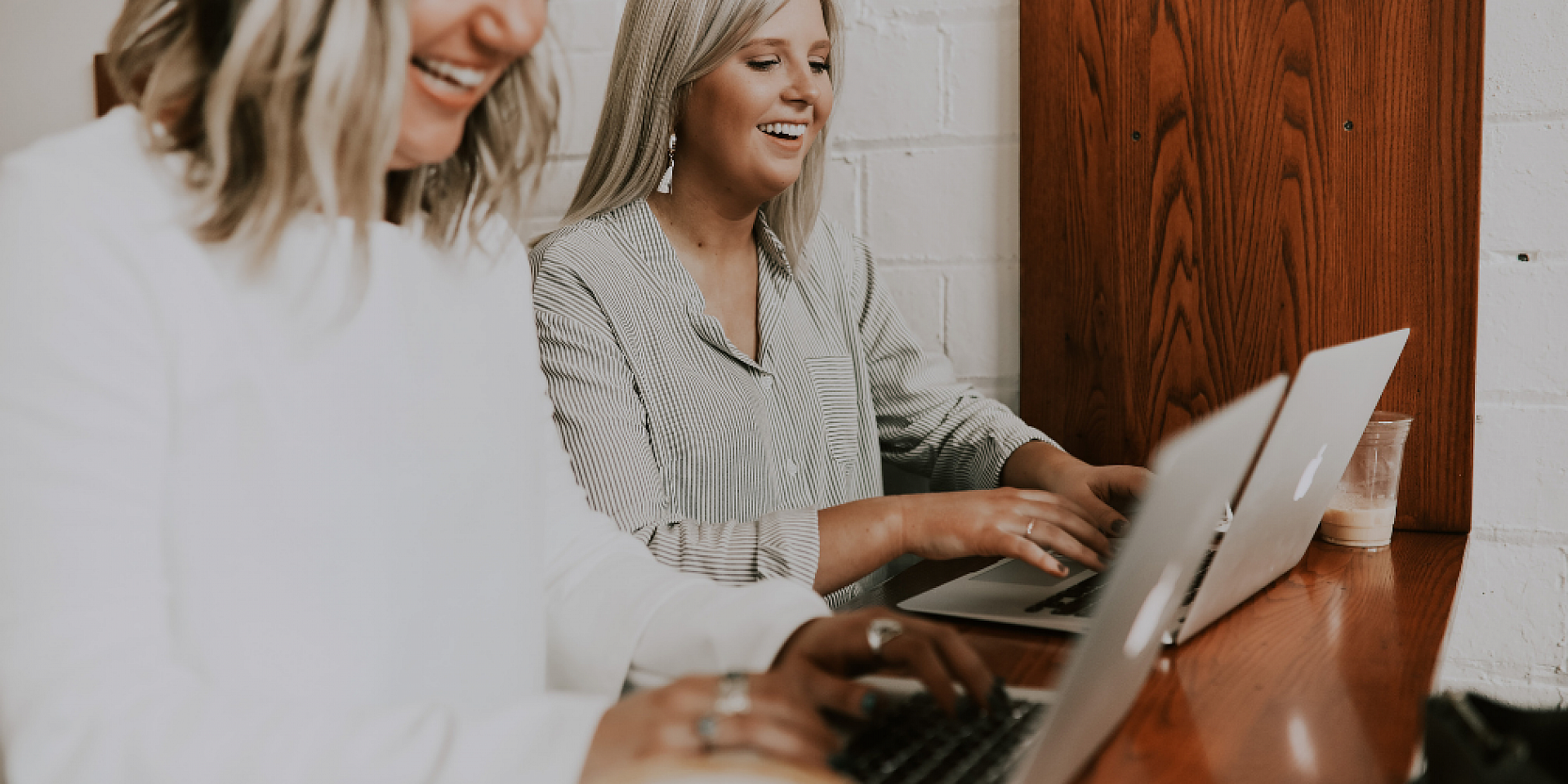 Two women smiling and working side-by-side on latops