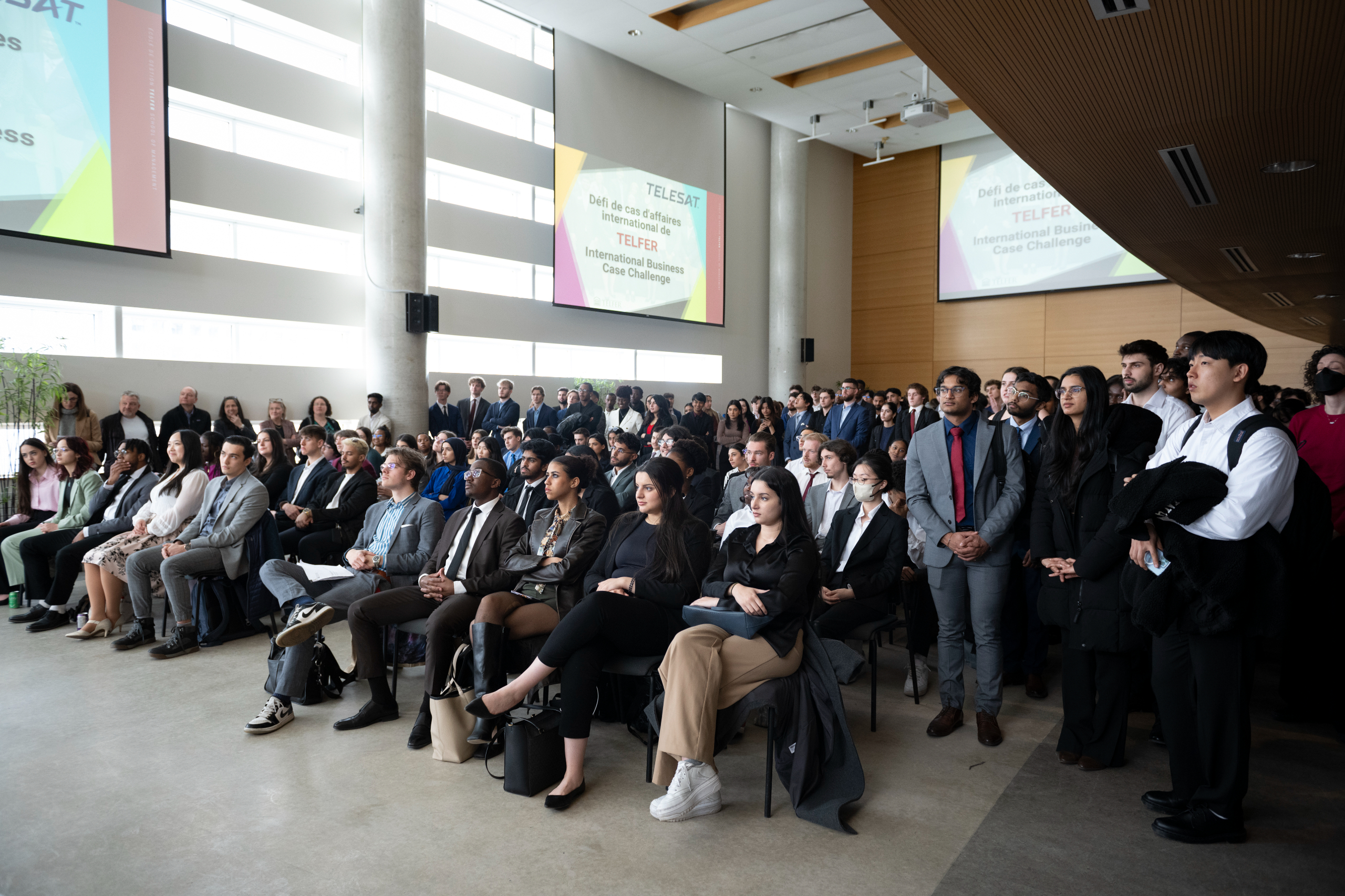 Un public varié d'étudiants écoutant attentivement une présentation lors d'un événement formel. 