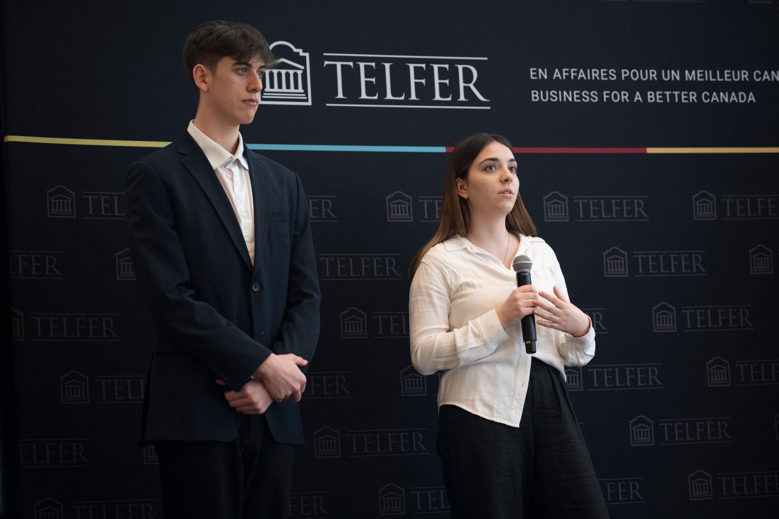 Two young professionals present at a case competition in front of a Telfer backdrop.