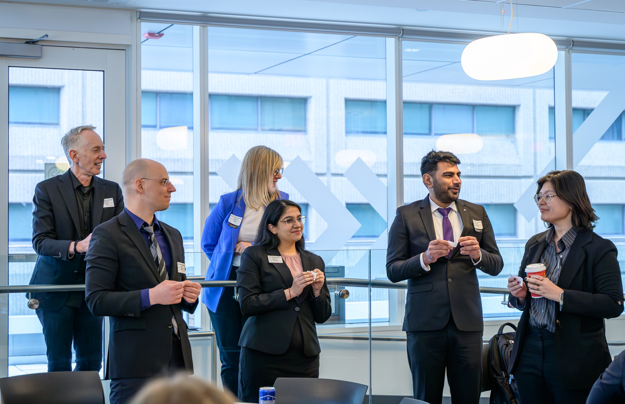 A diverse group of professionals stand and talk in a brightly lit room with large windows.  