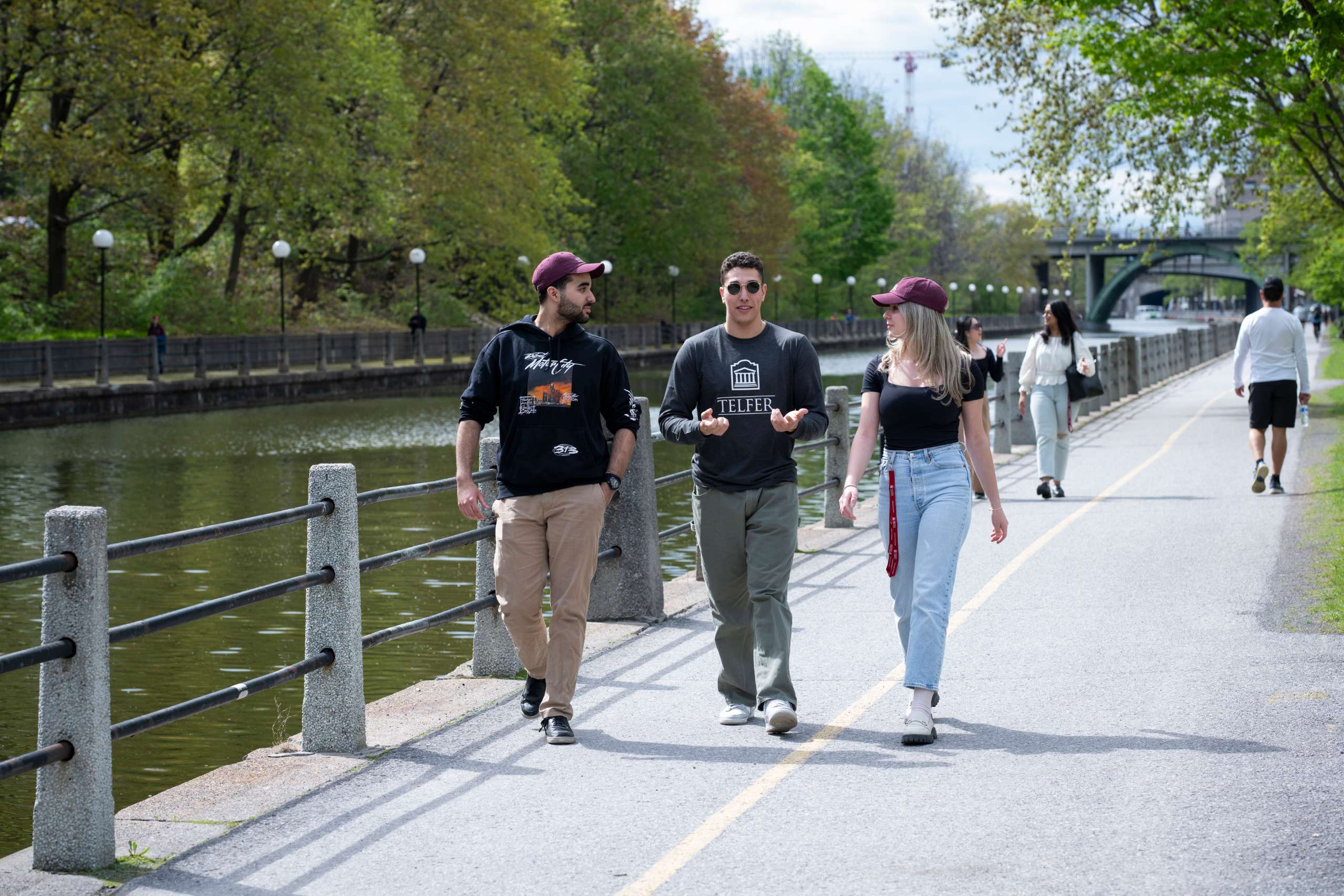 Three BCom students talk a walk outside along the Rideau Canal path while in discussion