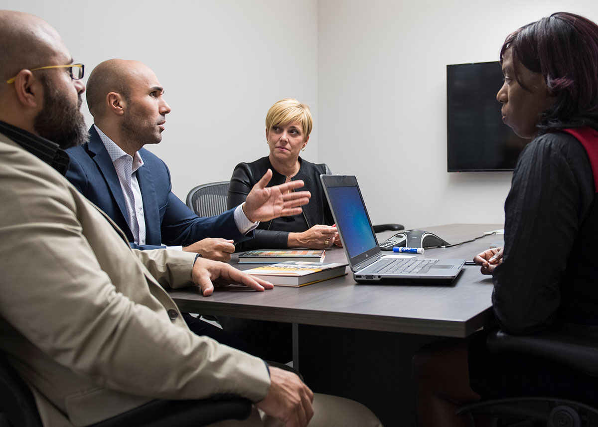 Photo d’un groupe de quatre personnes candidates au MBA pour cadres qui discutent d’un cas dans une salle d’études; photo originale.  