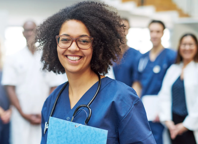 A young female doctor stands in front of a group of other doctors.