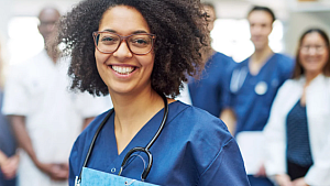 A young female doctor stands in front of a group of other doctors.