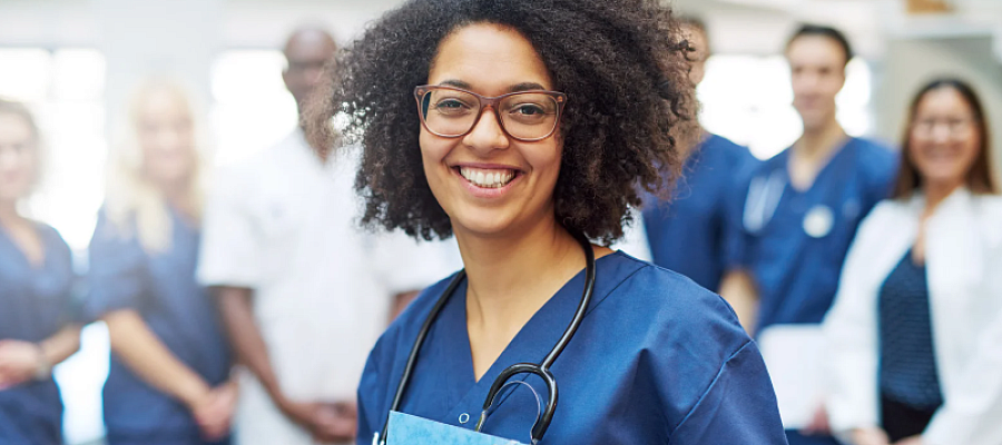 A young female doctor stands in front of a group of other doctors.