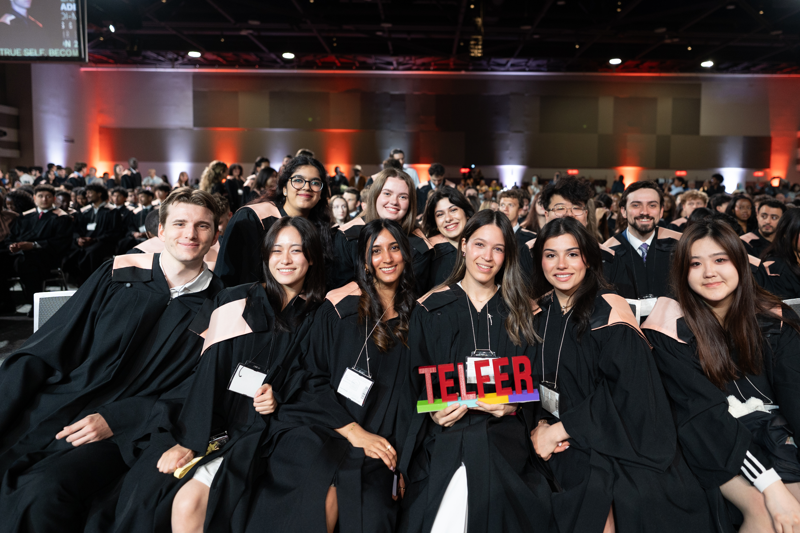 A group of students in graduation robes holding a mini telfer sign.