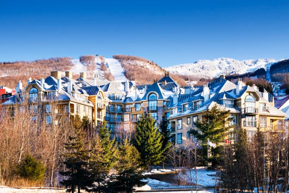 Exterior view of Le Westin Tremblant, a multi-level hotel, with trees in the foreground and the Mont Tremblant ski resort in the background.