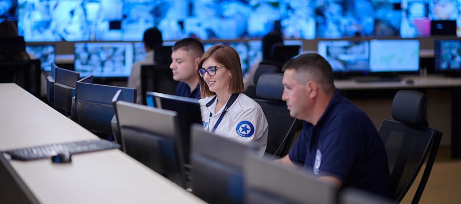 A woman works in a security office alongside two colleagues.