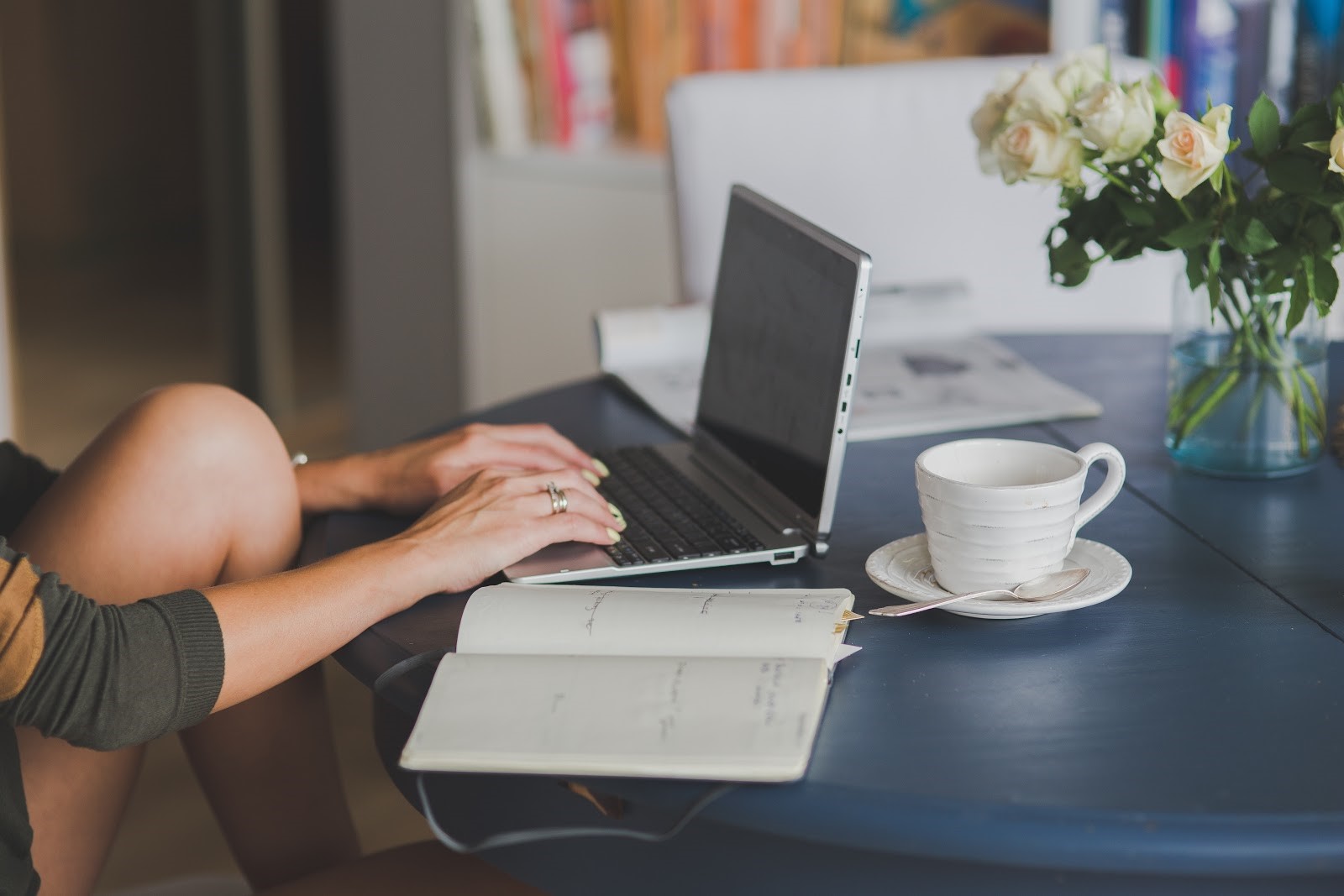 Mains de femme travaillant sur un ordinateur portable avec un cahier et un café