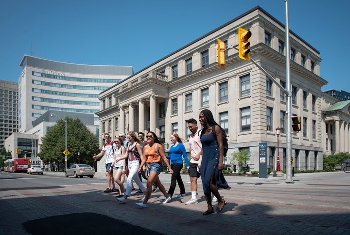 Groupe d'étudiants de Telfer traversant la rue et souriant sur le campus de l'Université d'Ottawa