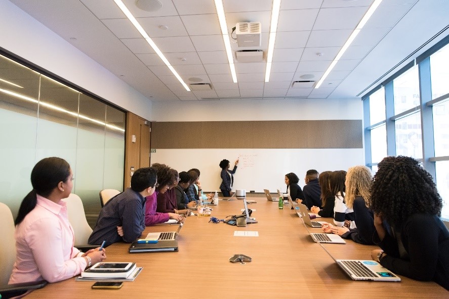 Des étudiants et étudiants autour d'une table de conférence qui écoute une professeure à l'avant au tableau